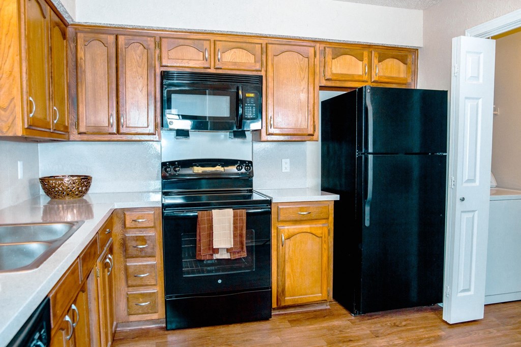 Kitchen with black appliances and wooden cabinets at Chisholm Place Apartments in Plano, TX