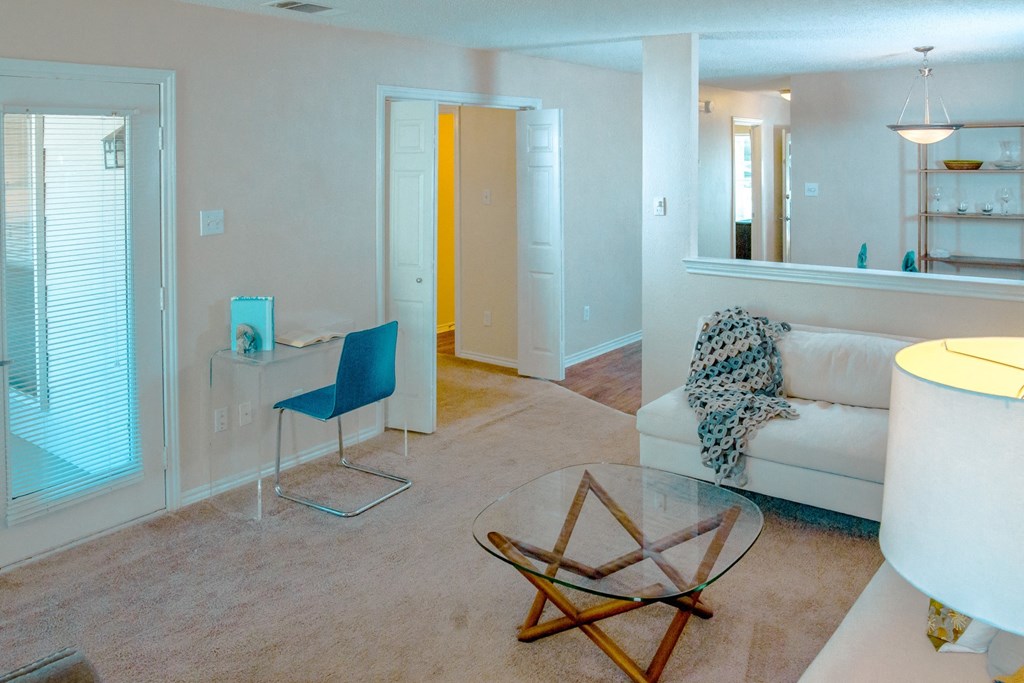 View of living room with a white couch, glass coffee table, and desk at Chisholm Place Apartments in Plano, TX