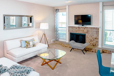 Model living room with a couch and a table and a fireplace at Chisholm Place Apartments in Plano, TX