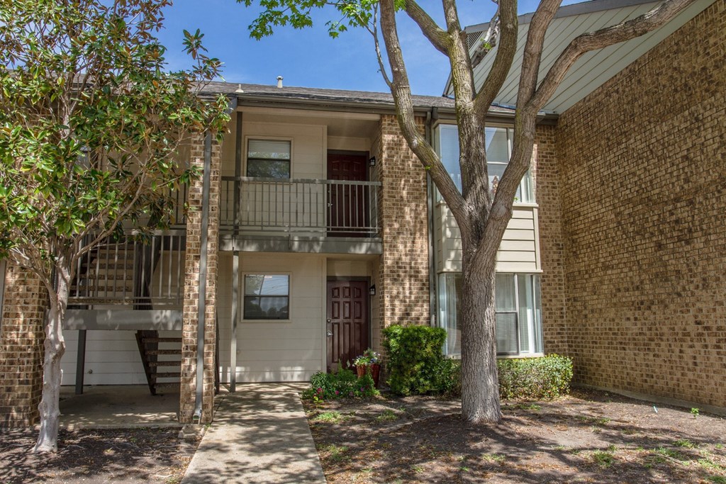 Front view of apartment building with trees and a pathway at Chisholm Place Apartments in Plano, TX