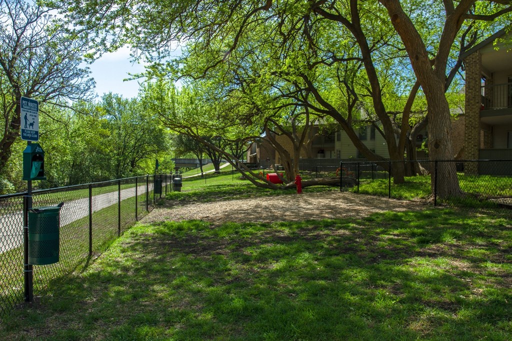 A fenced in dog park with trees at Chisholm Place Apartments in Plano, TX