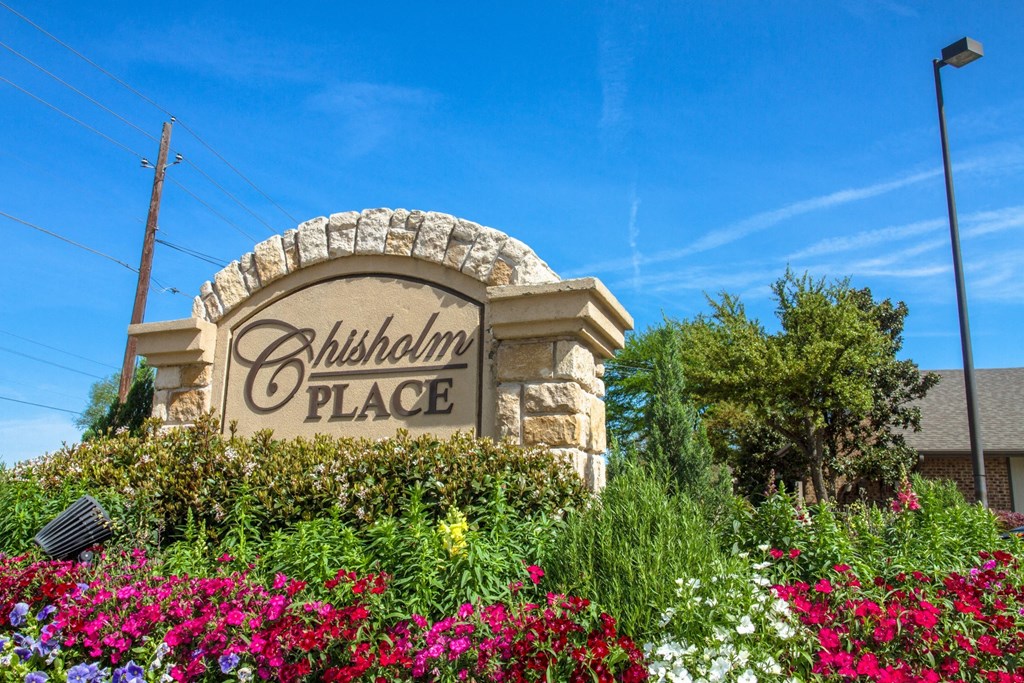 Property signage surrounded by a colorful flower bed at Chisholm Place Apartments in Plano, TX