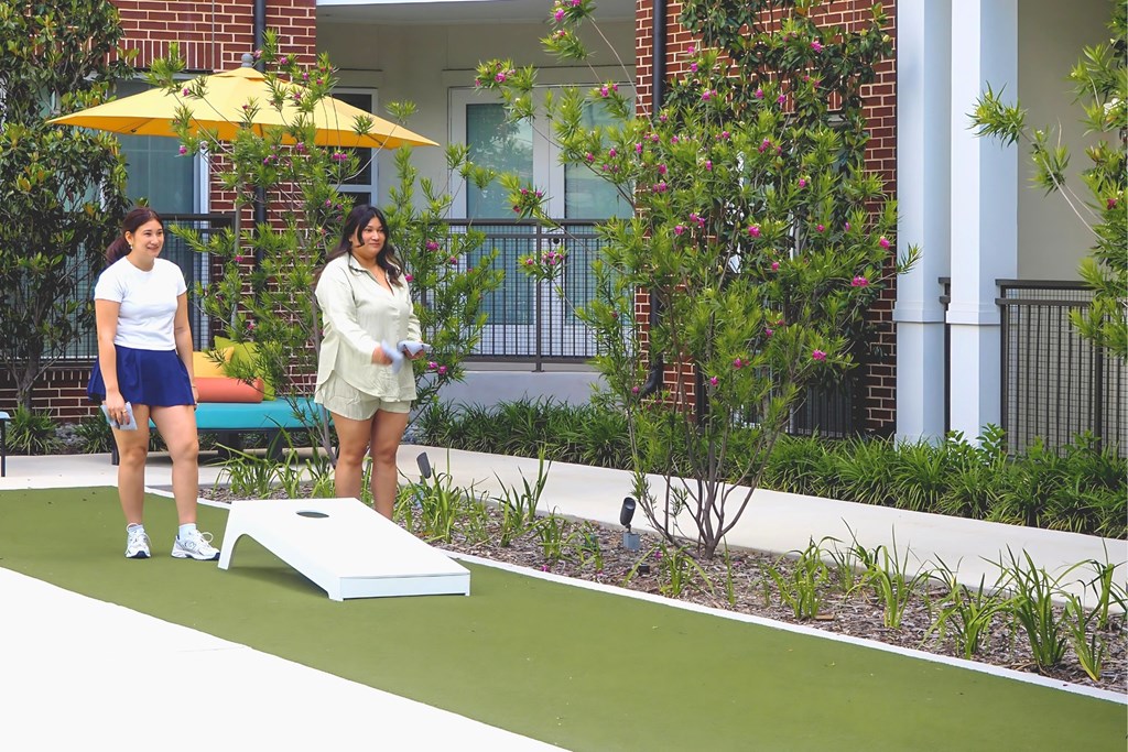 Two women playing cornhole in front of Apartments at Era in Denton TX.