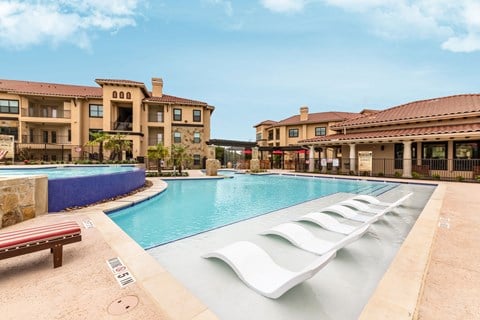 a large swimming pool with white lounge chairs in front of apartment buildings