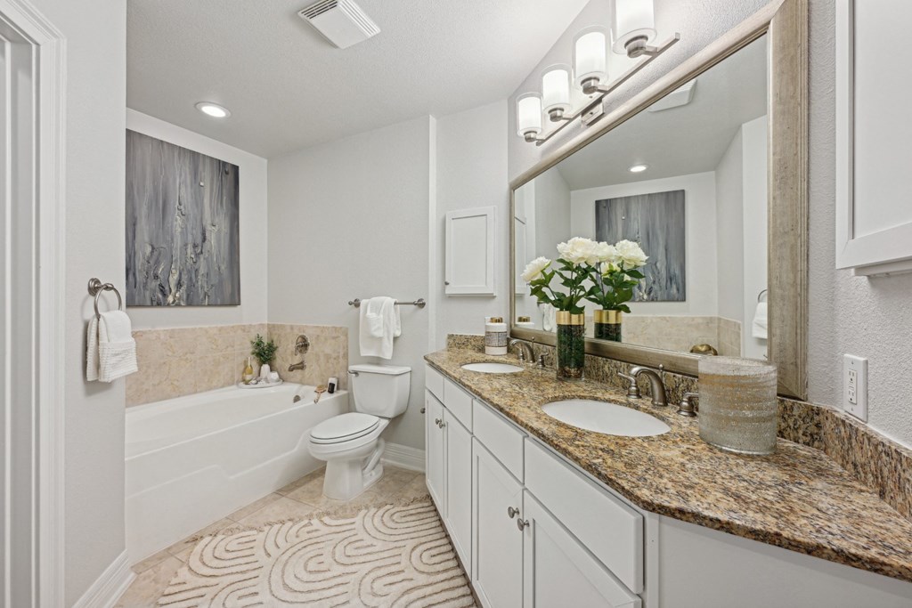 Model master bathroom with a toilet, sink, and a large mirror at Dominion Post Oak apartments in Houston, TX