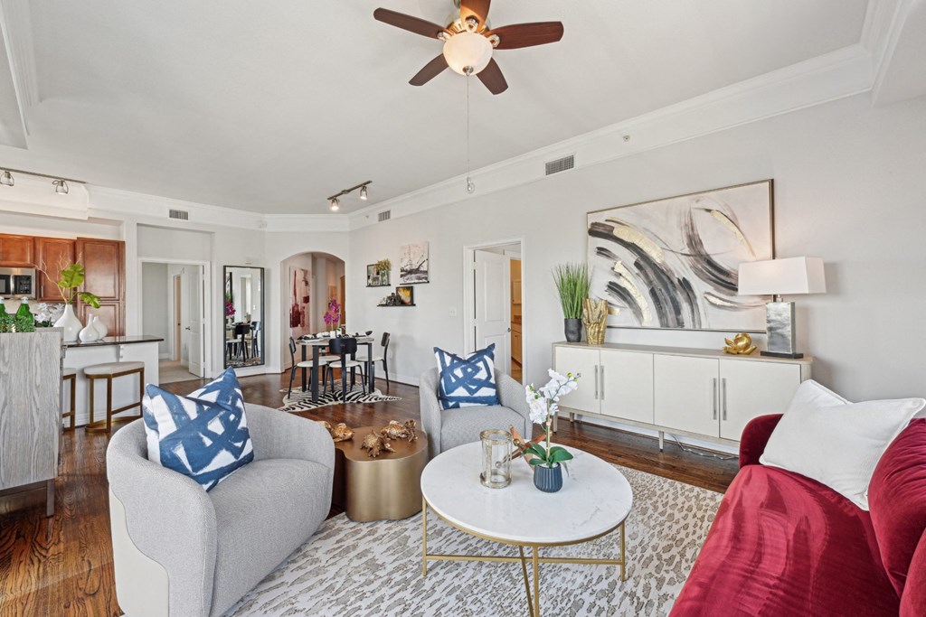 Model living room with a grey couch, a red couch, a white coffee table, and a ceiling fan at Dominion Post Oak apartments in Houston, TX
