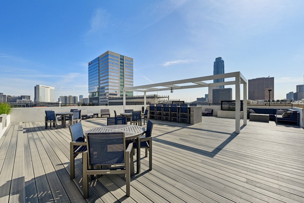 Wooden deck with chairs and a table with a metal frame on the rooftop patio at Dominion Post Oak apartments in Houston, TX
