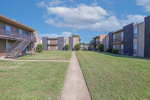A grassy area in front of apartment buildings with a concrete walkway at The Drake in Bossier City, LA