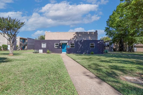 A laundry center with a blue door is surrounded by a grassy area and trees at The Drake in Bossier City, LA