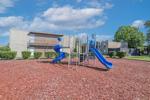 A playground with a blue slide and a red bark ground at The Drake in Bossier City, LA