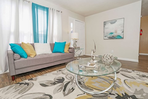 A living room with a grey couch and a glass coffee table at The Drake in Bossier City, LA