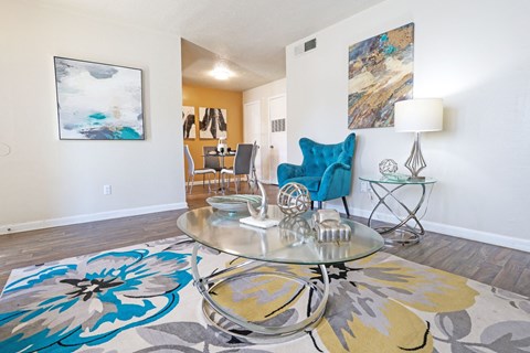 A living room with a glass coffee table and a blue chair at The Drake in Bossier City, LA