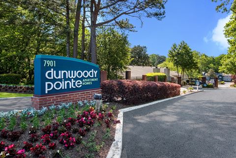 a sign for dunwoody pointe with flowers and bushes in front of it