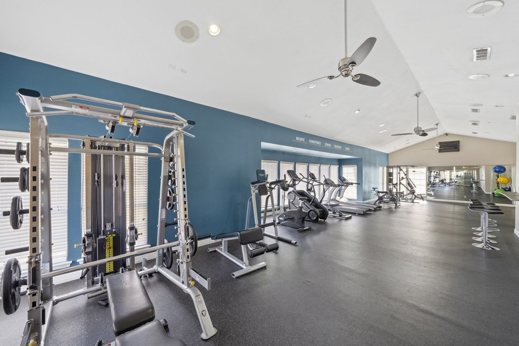 Fitness center with weights and cardio machines, squat rack, and ceiling fans at Davenport Apartments in Dallas, TX
