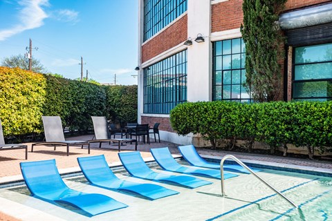 a swimming pool with blue lounge chairs in front of a building