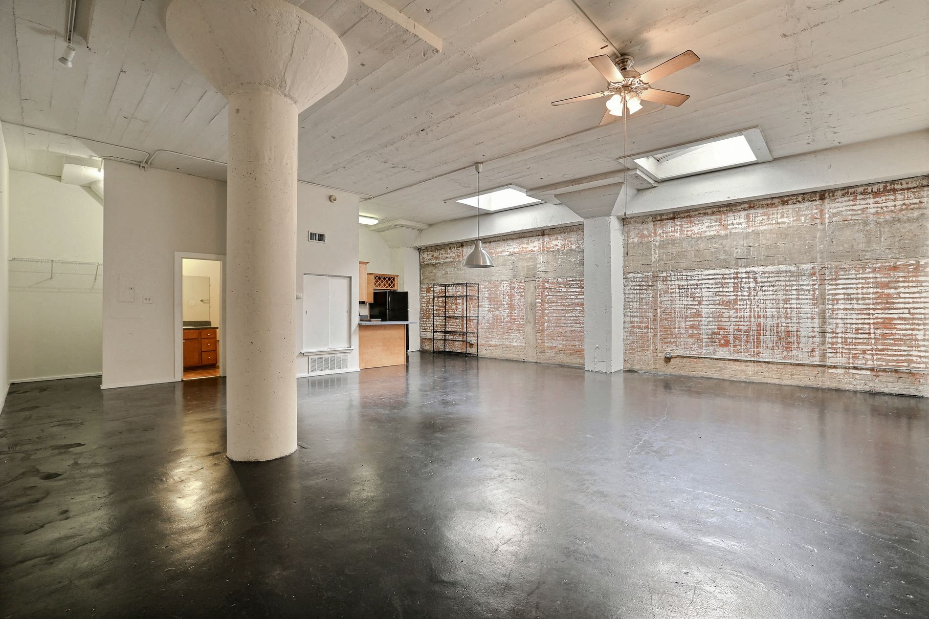 A large empty room with a ceiling fan and a brick wall.