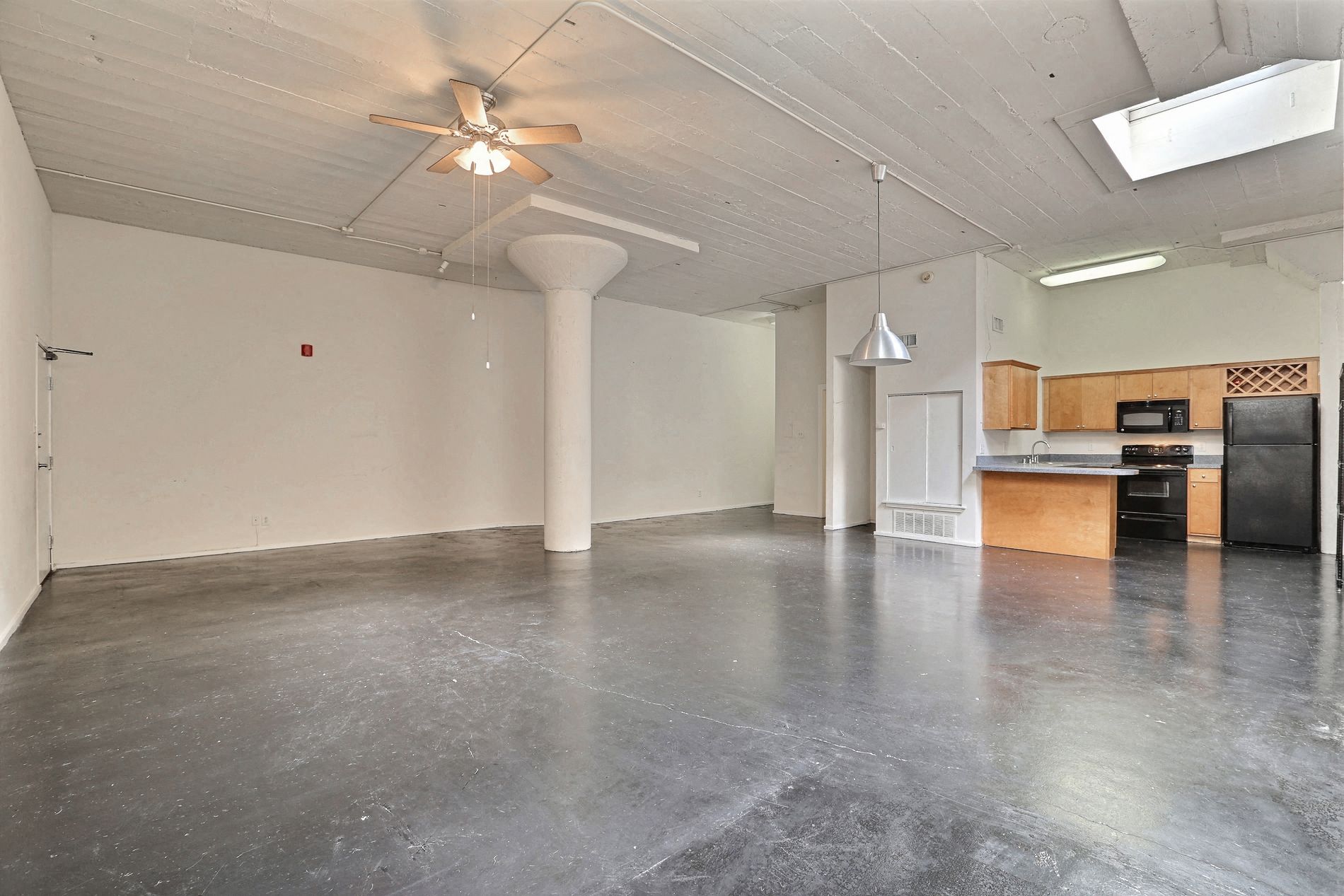 A spacious room with a ceiling fan and a kitchenette in the corner.