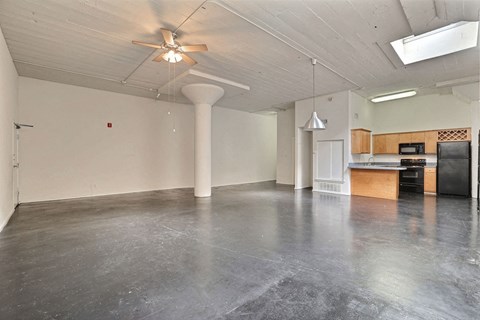 A spacious room with a ceiling fan and a kitchenette in the corner.