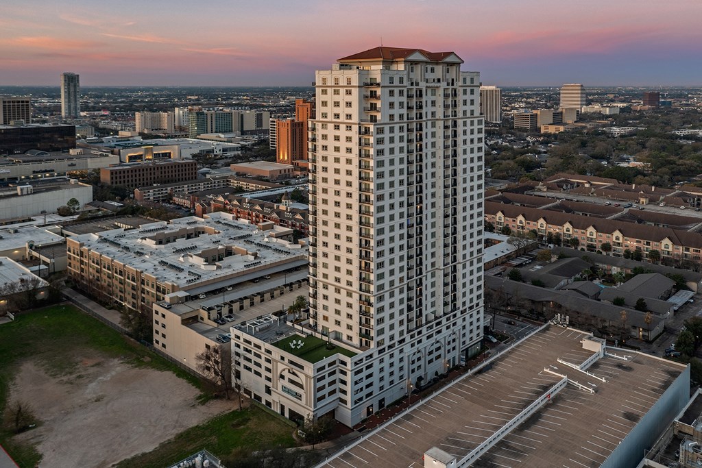 an aerial view of a tall building with a red roof and a parking lot in front of at Dominion Post Oak in Houston, TX