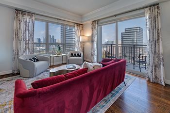 a living room with a red couch and a large window with a view of a city at Dominion Post Oak in Houston, TX
