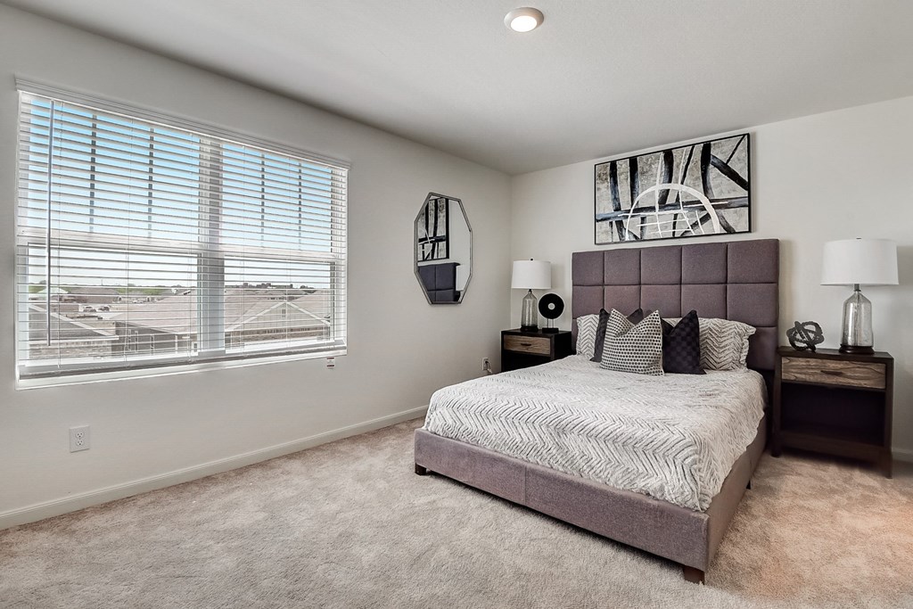 a model bedroom with carpet floor, big window and brown furnitures