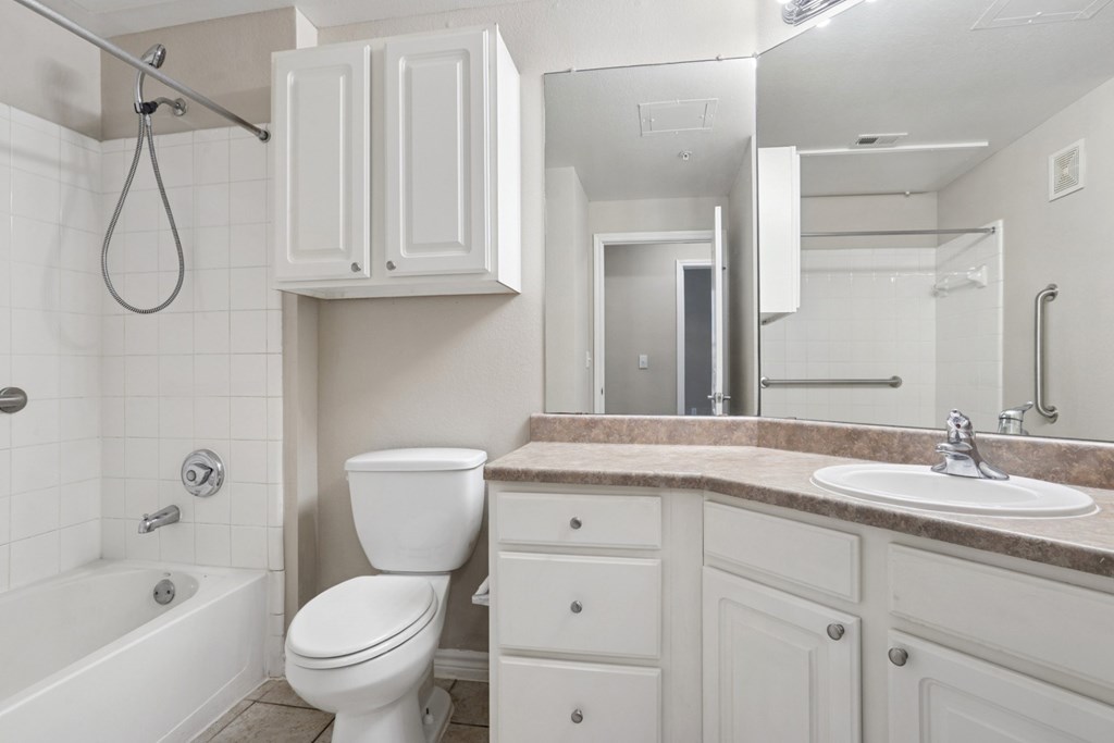 Edinburgh bathroom with a toilet, counter, sink, and mirror at Encore at Buckingham Apartments in Richardson, TX