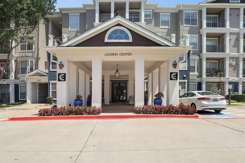 The entrance to the leasing office with white pillars and landscaping at Encore at Buckingham Apartments in Richardson, TX
