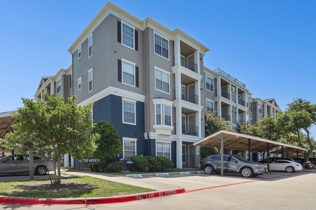 The exterior of the apartment complex with a parking lot in front at Encore at Buckingham Apartments in Richardson, TX