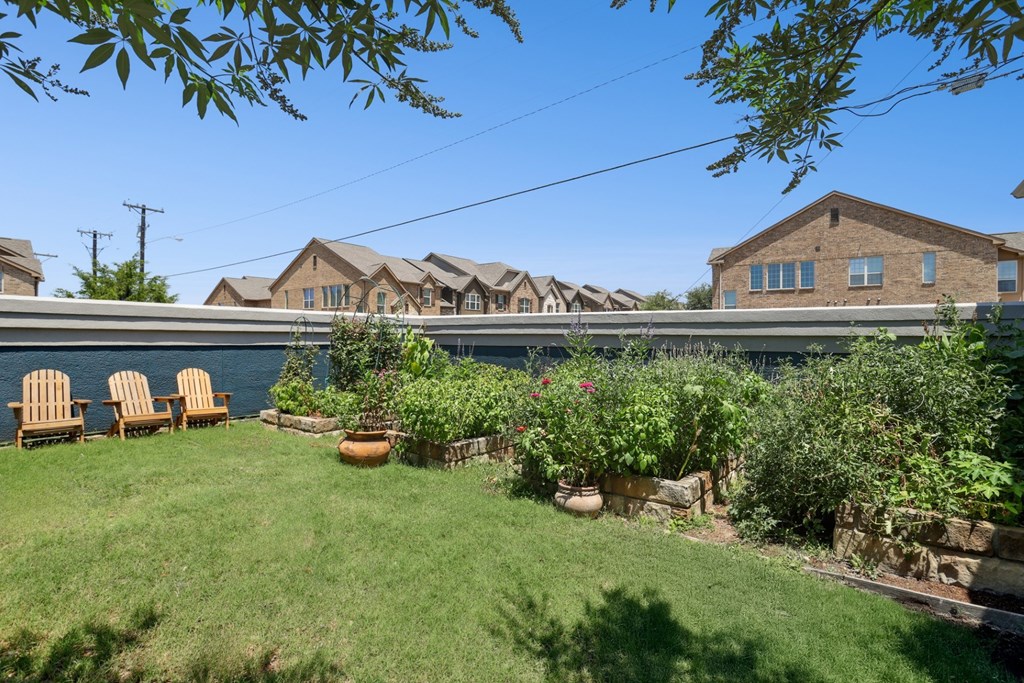 A lush garden with chairs and apartment buildings in the background at Encore at Buckingham Apartments in Richardson, TX