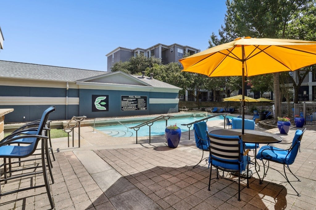 A pool area with chairs and a yellow umbrella at Encore at Buckingham Apartments in Richardson, TX