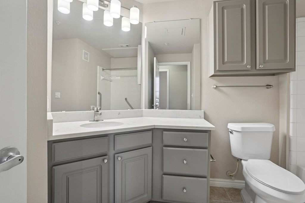 Kenzington bathroom with a white toilet and a sink with a mirror above it at Encore at Buckingham Apartments in Richardson, TX