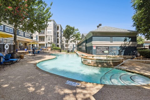 A sparkling swimming pool with apartment buildings in the background at Encore at Buckingham Apartments in Richardson, TX
