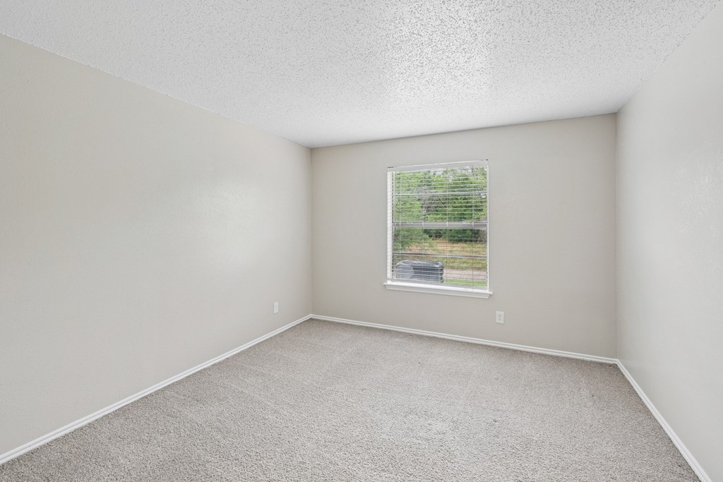 B1 carpeted bedroom with a window showing a view of trees at Estelle Creek North Apartments in Irving, TX