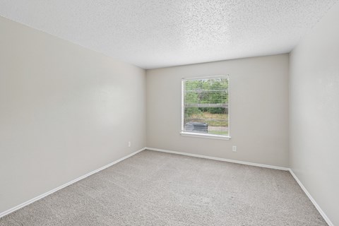 A room with a window showing a view of a road and trees.