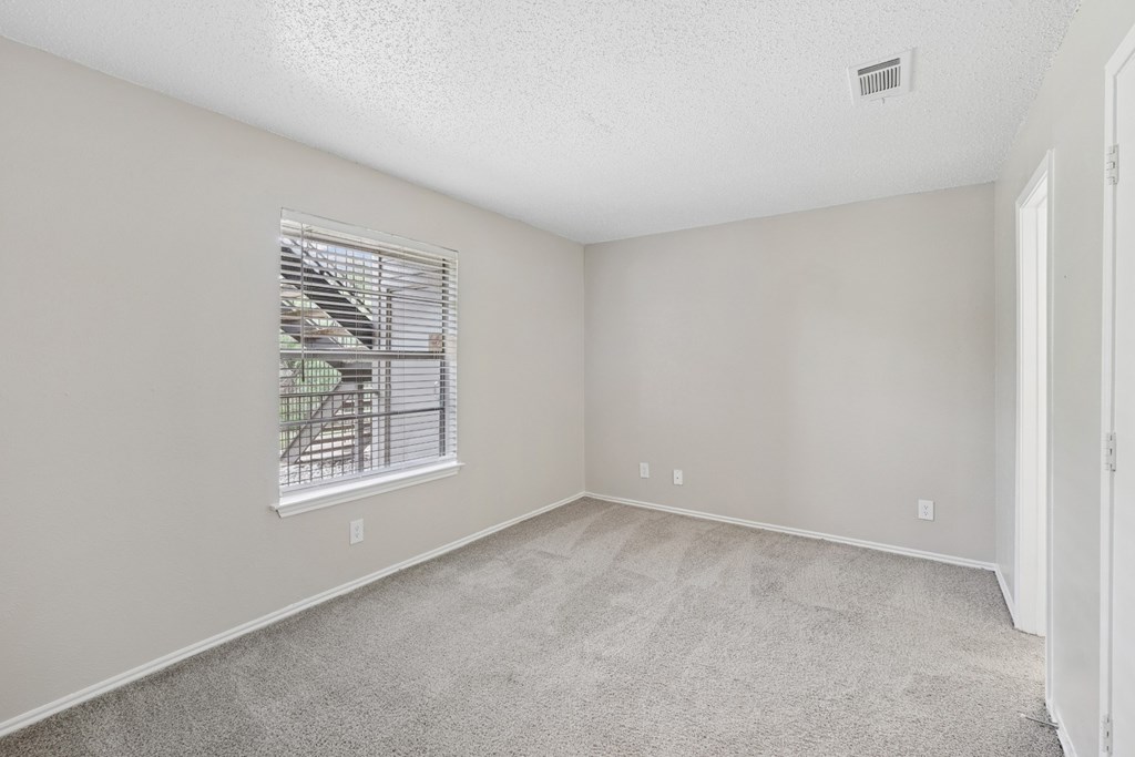 A bedroom with a window and carpeted floor at Estelle Creek North Apartments in Irving, TX