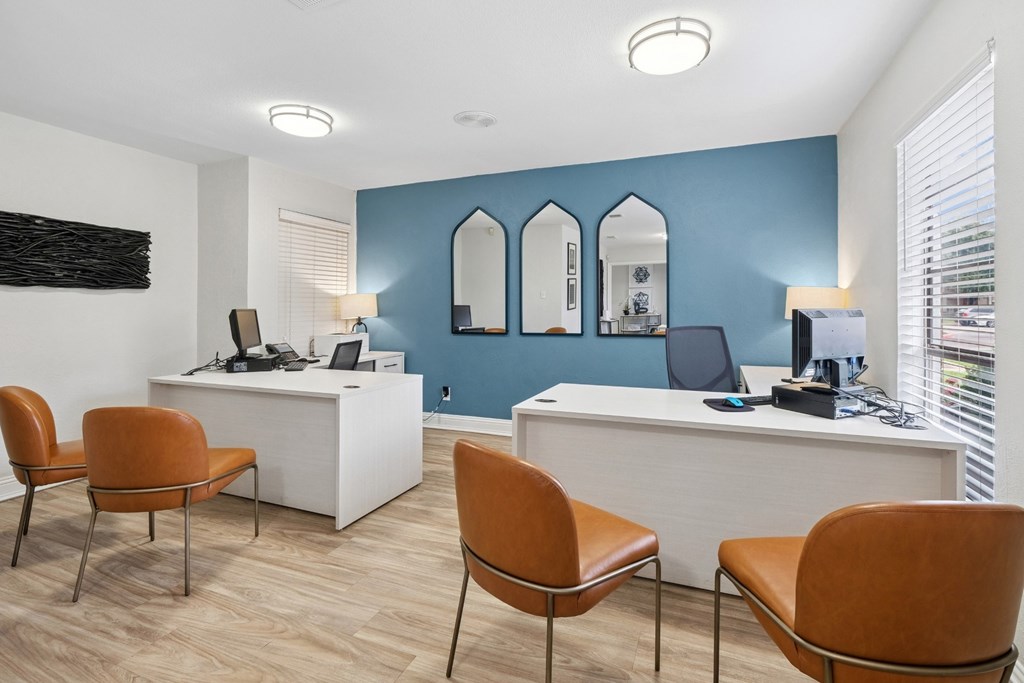 The interior of a leasing office with white desks and orange chairs at Estelle Creek North Apartments in Irving, TX