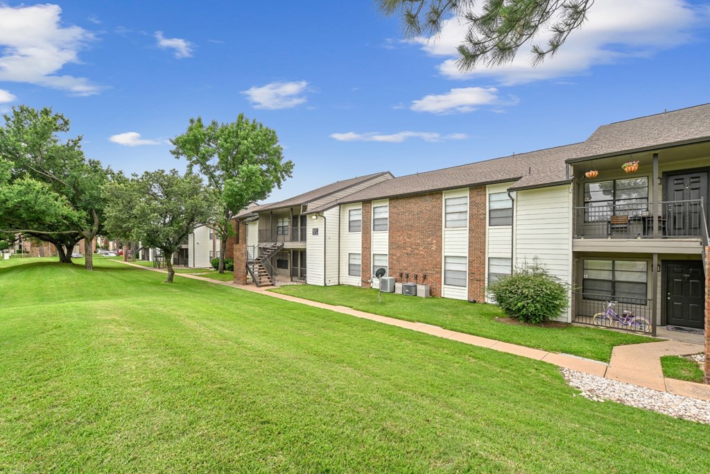 An exterior view of apartment buildings with a lush green lawn in front at Estelle Creek North Apartments in Irving, TX