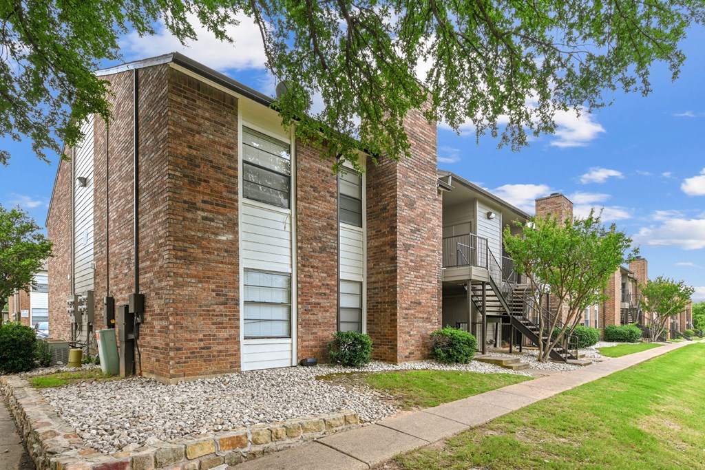 An apartment building with windows and a sidewalk in front at Estelle Creek North Apartments in Irving, TX