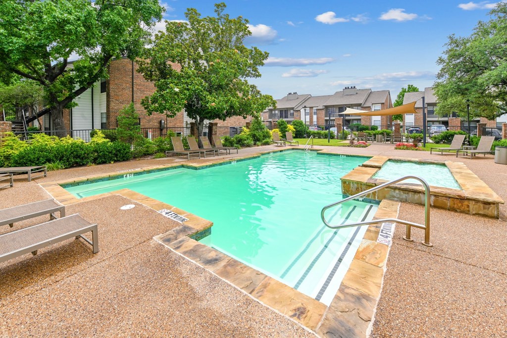 A swimming pool with comfortable lounge chairs and a waterfall feature at Estelle Creek North Apartments in Irving, TX