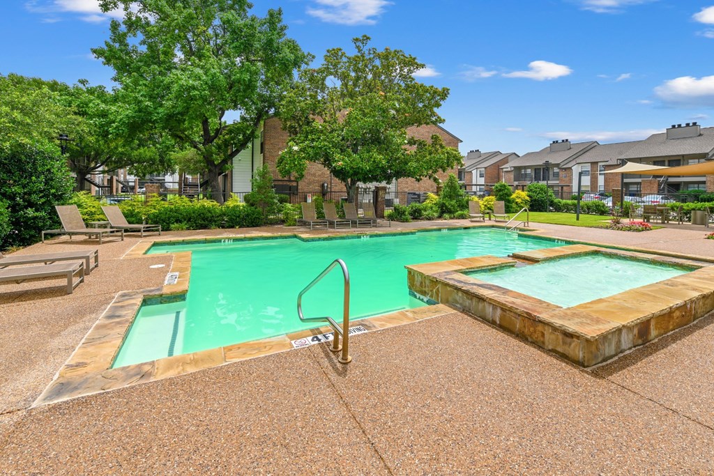 A swimming pool with a waterfall feature and lush trees in the background at Estelle Creek North Apartments in Irving, TX