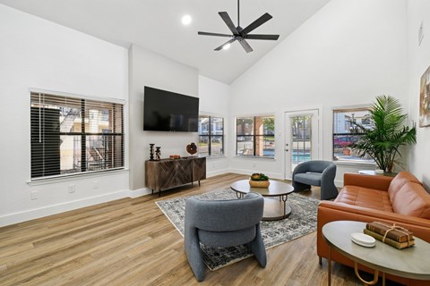 A living room with a grey armchair, a brown leather couch, a wooden coffee table, and a flat screen TV mounted on the wall.