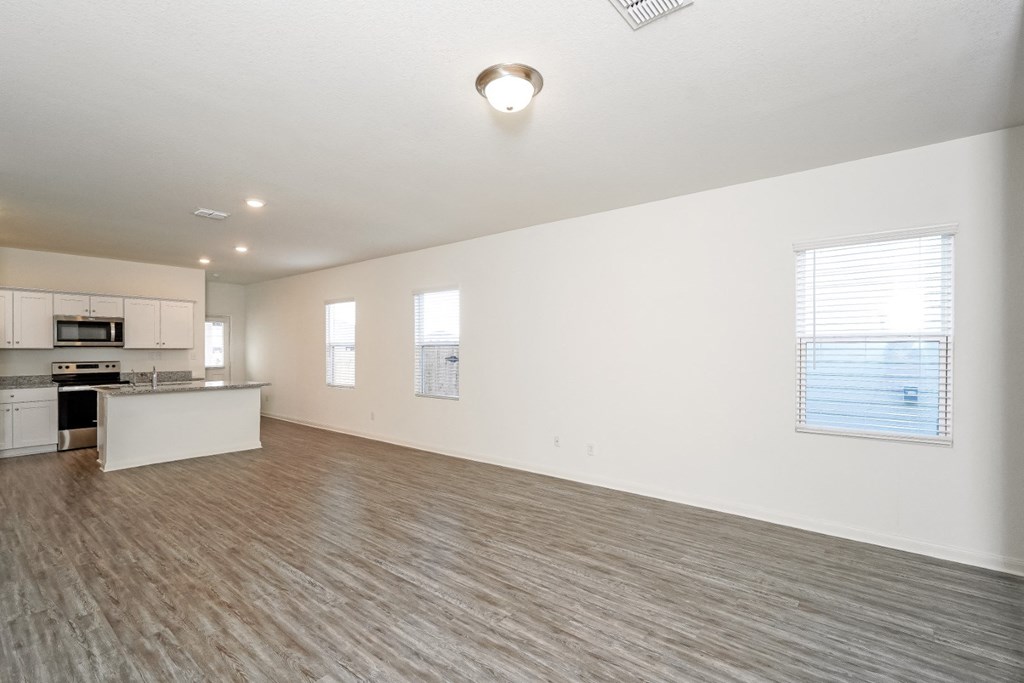 an empty living room with a kitchen in the background