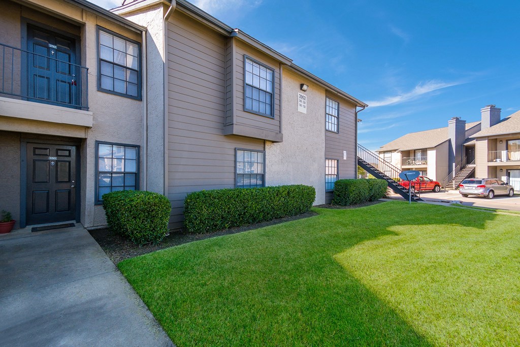 an apartment building with a green lawn and a sidewalk