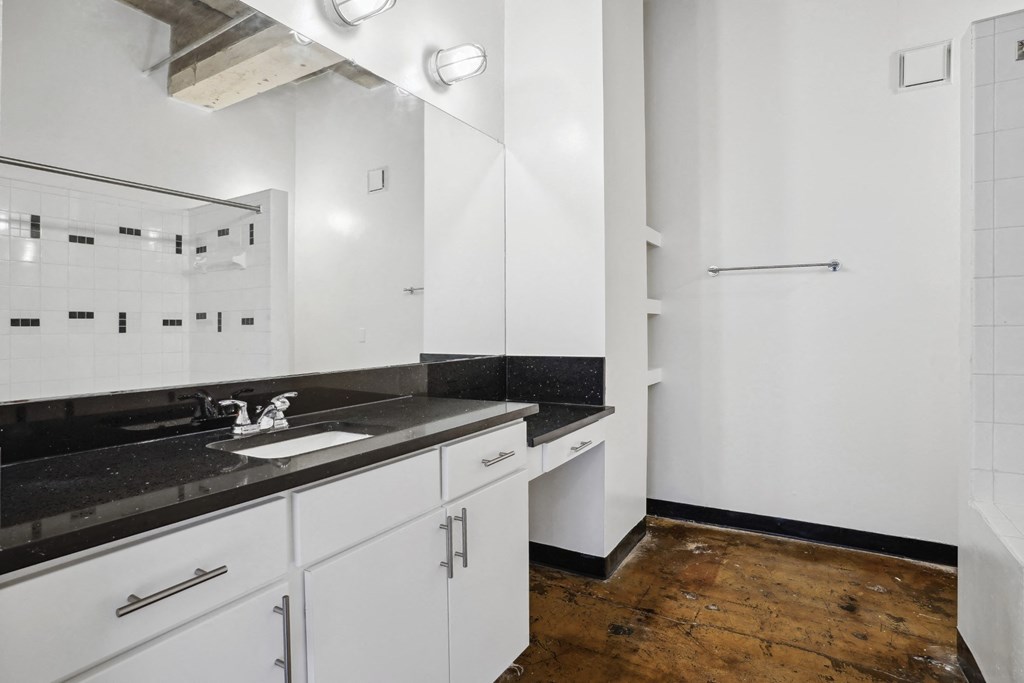 Farm and Ranch spacious bathroom with soaking shower tub, modern black countertop vanity, and built-in shelving | Deep Ellum Lofts in Dallas, TX