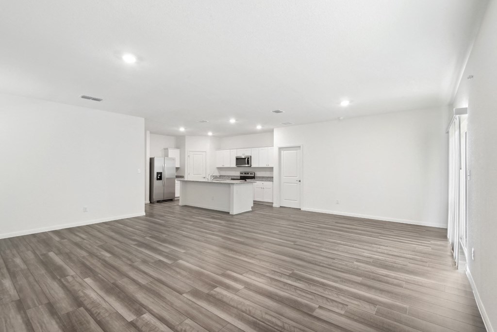an empty living room with a kitchen in the background