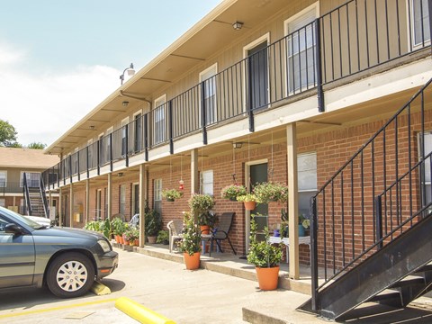 A car is parked in a yellow line in front of a building with a balcony.