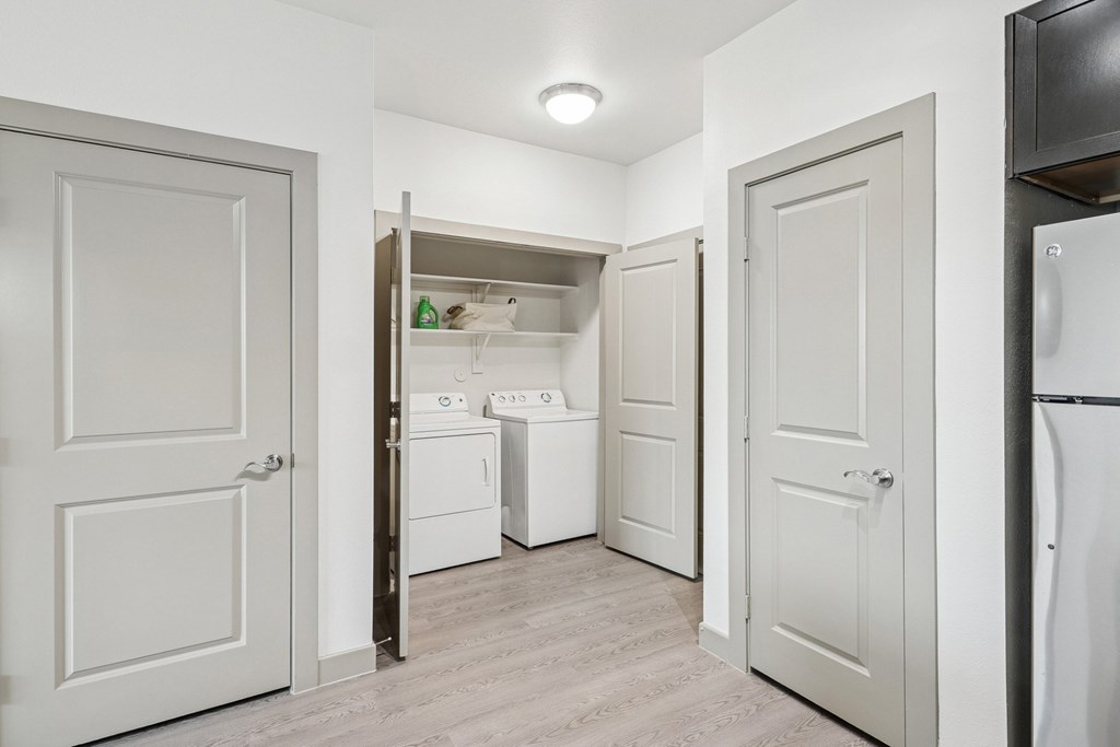 A dedicated laundry space with a full size washer and dryers and shelves at GreenVue Apartments in Richardson, TX