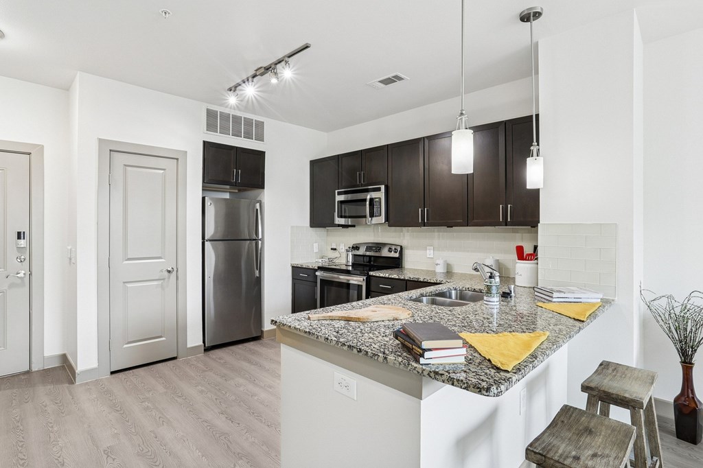 A modern kitchen with stainless steel appliances, a brick backsplash, and dark cabinets at GreenVue Apartments in Richardson, TX