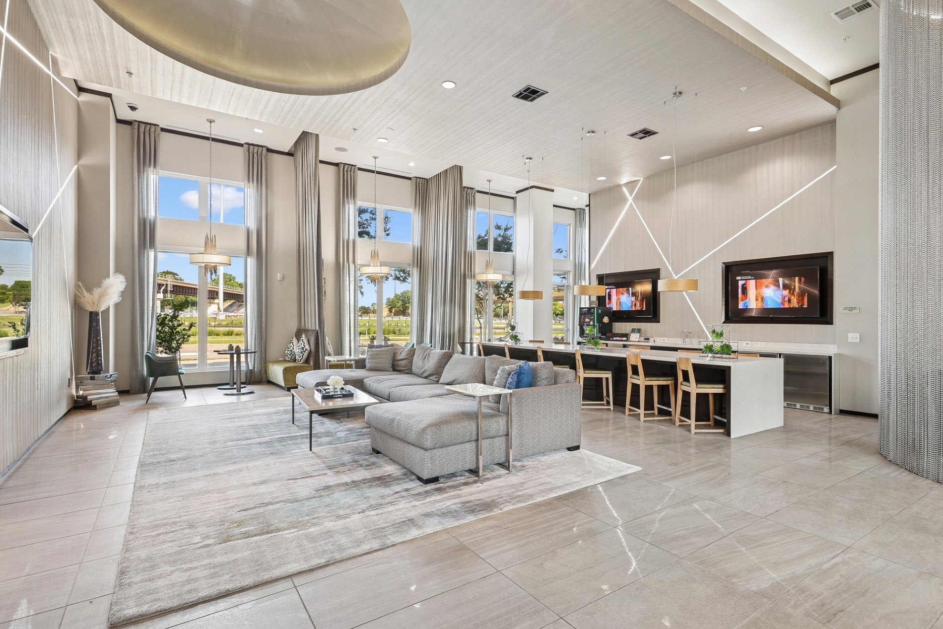 A modern living room with a grey sofa set and a white kitchen area.