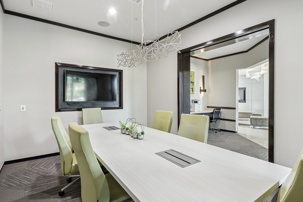 A modern conference room with a long table, chairs, and a television at GreenVue Apartments in Richardson, TX
